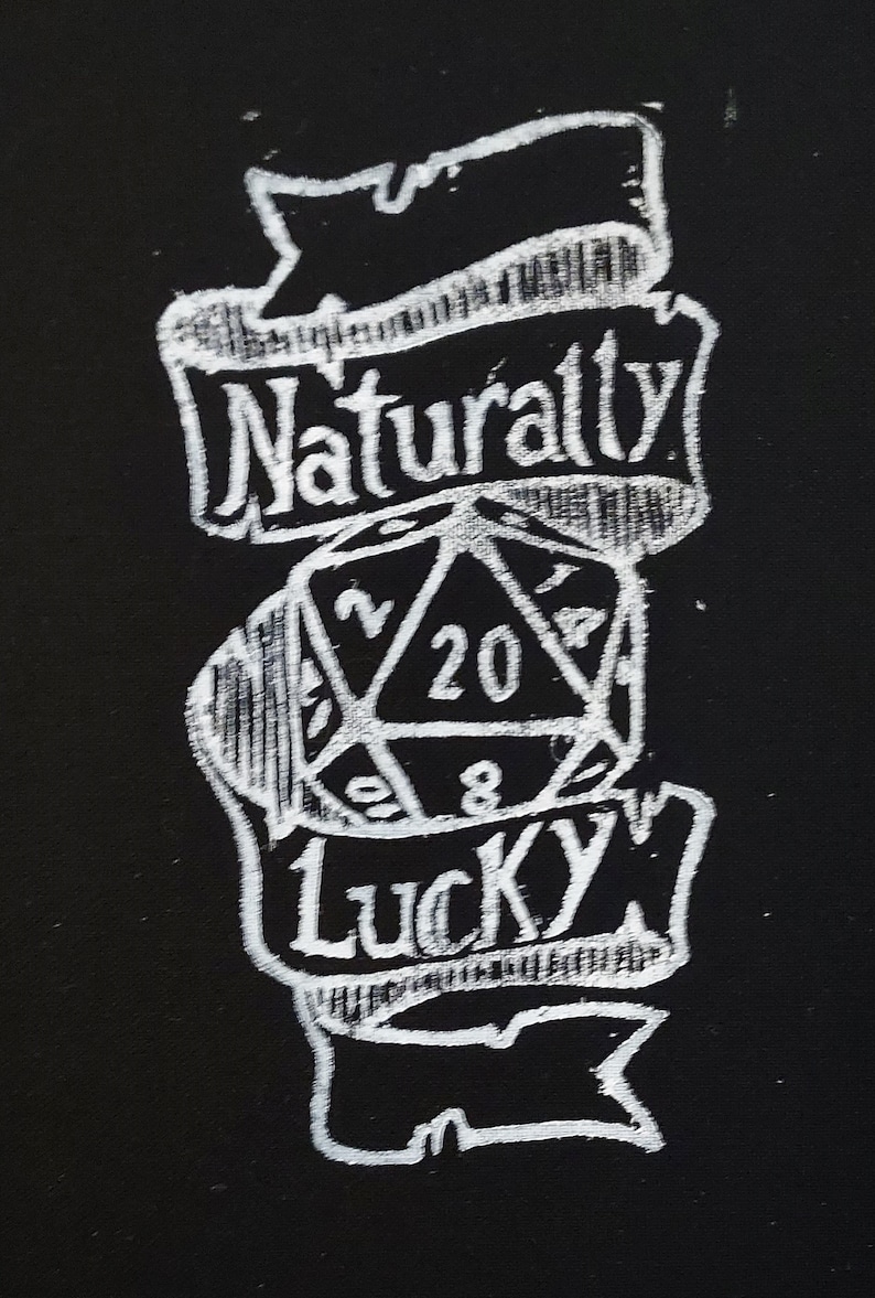 K&ouml;nnte beinhalten: Eine Schwarzwei&szlig;illustration eines zwanzigseitigen W&uuml;rfels mit den Worten "Naturally Lucky" auf einem Banner dar&uuml;ber.