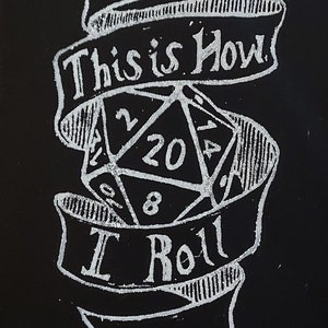 K&ouml;nnte beinhalten: Eine wei&szlig;e Tintenillustration auf schwarzem Hintergrund eines zwanzigseitigen W&uuml;rfels mit dem Text "This is How I Roll" auf einem Banner.