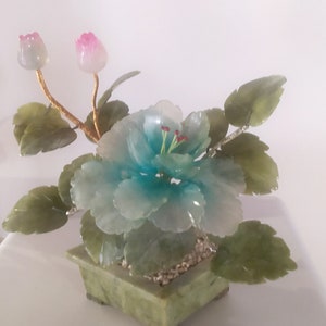May include: A jade flower arrangement featuring a blue and white flower, two pink buds, and green leaves. The arrangement is displayed in a green jade pot.