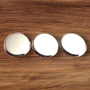 May include: Three round, clear glass objects with a silver metal rim. The objects are arranged in a row on a wooden surface. The glass has a slightly frosted appearance.