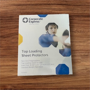 May include: A package of "Corporate Express" top-loading sheet protectors. The white package has blue and yellow accents and features a woman's image. The text reads "Top Loading Sheet Protectors" and lists the insert size as 8-1/2" x 11".