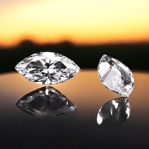 May include: Two clear, faceted marquise-shaped diamonds on a black reflective surface. The diamonds are reflecting light and have a brilliant sparkle.