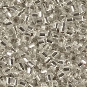 May include: A close-up image of a large quantity of small, clear glass seed beads. The beads are cylindrical in shape and have a slight iridescent sheen.