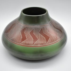 Peut inclure: Un pot en céramique vert avec un motif géométrique rouge et blanc. Le pot est rond et a une large ouverture.