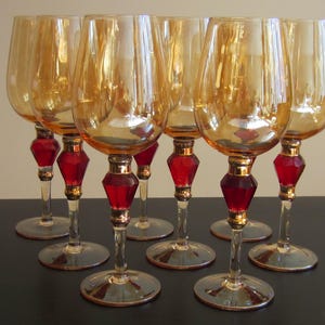 May include: Set of eight amber glass wine glasses with red and gold accents. The glasses have a round bowl and a tall stem.