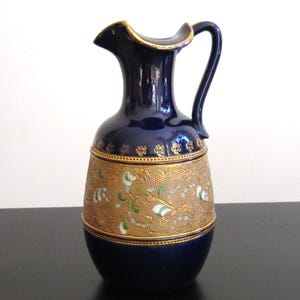 May include: A cobalt blue ceramic jug with a gold and white floral design. The jug has a wide mouth and a handle.