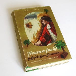 以下が含まれることがあります： ロバート・ルイス・スティーブンソン著「宝島」のヴィンテージハードカバー本。本の表紙には、赤いジャケットを着た少年が、背景に船が見える熱帯の島に立っている様子が描かれている。この本は「The Heirloom Library」シリーズの一部であり、ワーナー・シュタインによってイラストが描かれている。