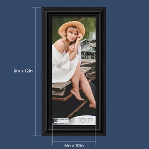 May include: A black framed photo of a woman wearing a straw hat and a white dress sitting on a wooden dock. The photo is 6 inches by 12 inches and the frame is 4 inches by 10 inches. The photo is titled "Frames of Mind" and is made in the USA.