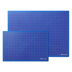 May include: Two blue self-healing cutting mats with a grid pattern and diagonal lines. The smaller mat is 12x18 inches and the larger mat is 18x24 inches. Both mats have "The Art Institute" printed on them.