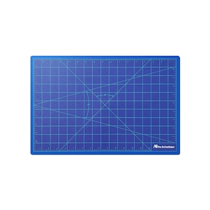 May include: Blue self-healing cutting mat with a grid pattern and ruler markings. The mat has a diagonal line pattern and a small circle with arrows indicating a 45-degree angle. The mat is labeled "The Art Institutes".