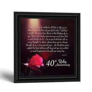 May include: A square black framed wall art piece featuring a dark background with a single pink rose at the bottom left. The text reads: What a time to celebrate all that in life you've shared since the time of your first date! 40th Ruby Anniversary.