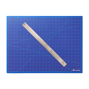 May include: A blue self-healing cutting mat with a silver ruler on top. The mat has a grid pattern and is marked with inches. The ruler is marked with inches and centimeters. The mat has the text "The Art Institutes" printed on the bottom right corner.