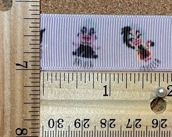 Pode incluir: Um close-up de uma fita branca com um padrão repetido de personagens de desenhos animados. A fita é medida com uma régua, mostrando que tem aproximadamente 2,5 cm de largura.