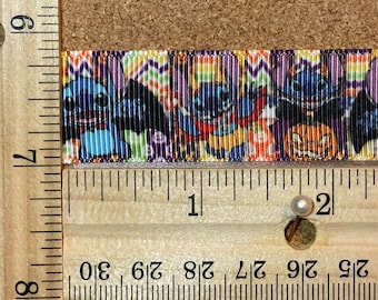 Pode incluir: Um close-up de uma fita colorida com um padrão repetido de personagens Stitch vestidos de vampiros. A fita é medida com uma régua de madeira, mostrando que tem aproximadamente 5 cm de comprimento.