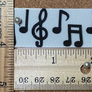 May include: A white ribbon with black musical notes printed on it. The ribbon is measured with a ruler, showing it is about 5 cm long.