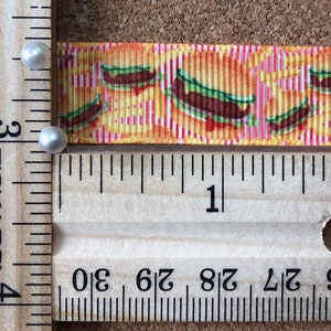 May include: A decorative ribbon featuring a repeating pattern of cartoon hamburgers. The ribbon is approximately 1 inch wide and is measured with a wooden ruler. The background is a corkboard.
