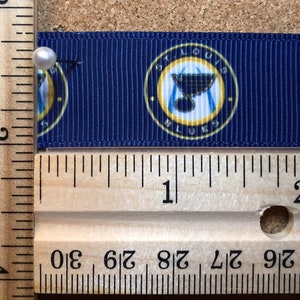 Pode incluir: Close-up de uma fita azul e amarela com as palavras "St. Louis Blues" impressas nela. A fita &eacute; medida com uma r&eacute;gua de madeira.