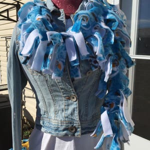May include: A blue and white fleece scarf with a pattern of cartoon characters. The scarf is tied around the neck of a denim jacket.