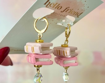 May include: Pink and white book-shaped earrings with gold accents and crystal drops. The earrings are hanging from gold hoops.