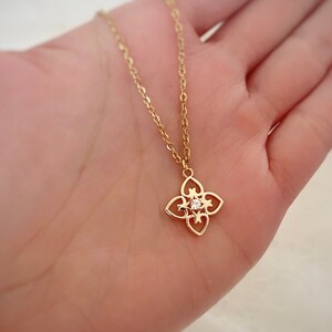 May include: A gold chain necklace with a delicate pendant featuring a four-leaf clover design with a small clear stone in the center.