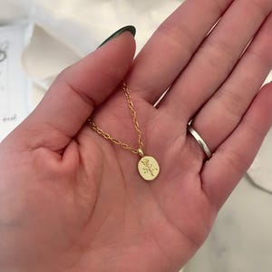 K&ouml;nnte beinhalten: Eine zarte, goldfarbene Halskette mit einem kleinen, ovalen Anh&auml;nger mit einem Rosendesign. Die Kette ist d&uuml;nn und der Anh&auml;nger ist etwa 1,3 cm lang. Die Halskette wird vor einem weichen, neutralen Hintergrund gezeigt.