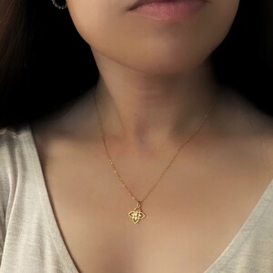 May include: A gold chain necklace with a small, intricate pendant featuring a four-pointed star design with clear stones.