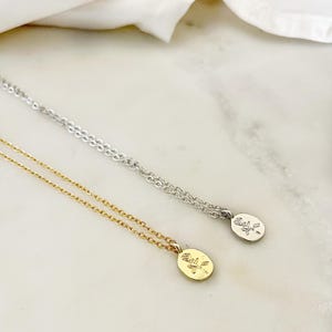 K&ouml;nnte beinhalten: Zwei zarte Halsketten mit ovalen Anh&auml;ngern mit einem Rosendesign. Eine Halskette ist goldfarben, die andere silberfarben. Beide Halsketten werden auf einer wei&szlig;-grauen Marmoroberfl&auml;che pr&auml;sentiert.