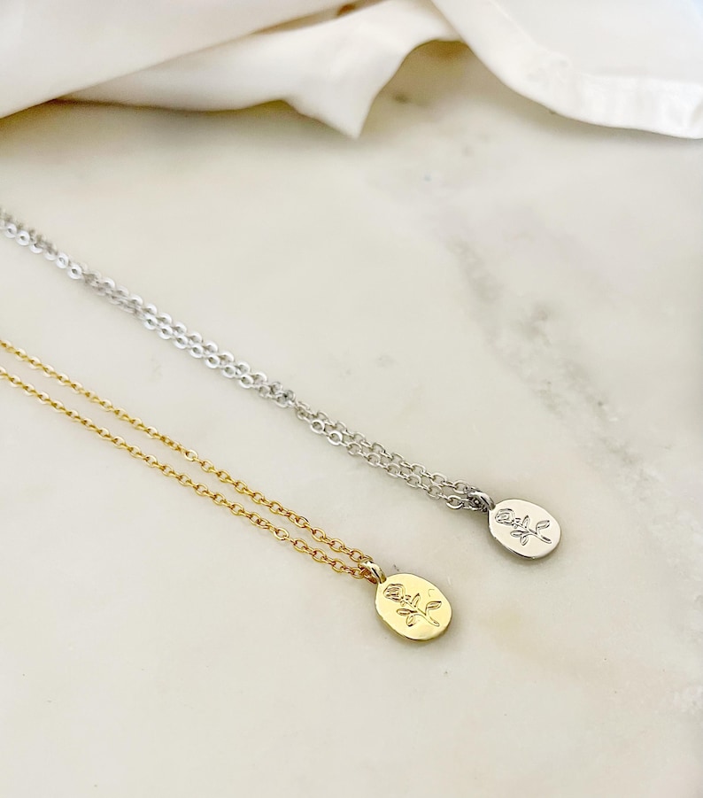 K&ouml;nnte beinhalten: Zwei zarte Halsketten mit ovalen Anh&auml;ngern mit einem Rosendesign. Eine Halskette ist goldfarben, die andere silberfarben. Beide Halsketten werden auf einer wei&szlig;-grauen Marmoroberfl&auml;che pr&auml;sentiert.
