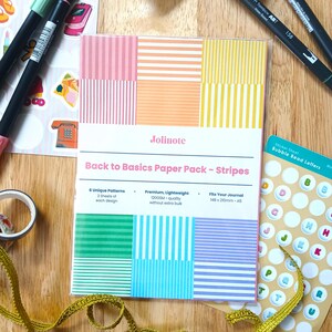 May include: A rectangular paper pack labeled Jolinote Back to Basics Paper Pack - Stripes, featuring six colorful striped patterns. The pack includes 120GSM paper measuring 148 x 210mm, or A5 size, with two sheets of each design for journaling.