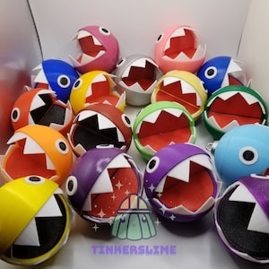 May include: A collection of colorful, spherical toy figures with open mouths and sharp teeth. The toys are in various colors including red, yellow, blue, and purple. Each figure has a white mouth and black eye details.