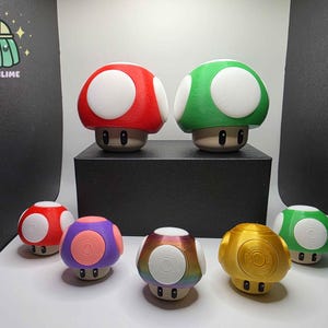 Puede incluir: Una colección de figuras con forma de hongo de varios colores, incluyendo rojo, verde, morado y dorado, con acentos circulares blancos. Las figuras se exhiben sobre una plataforma negra y una superficie blanca.