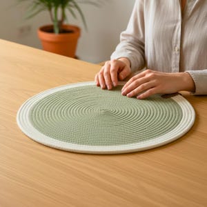 Könnte beinhalten: Ein runder, gewebter Platzdeckchen mit hellgrüner Mitte und weißem Rand. Der Platzdeckchen besteht aus einem dicken, strukturierten Material und liegt auf einem Holztisch. Der Durchmesser des Platzdeckchens beträgt ca. 30 cm.