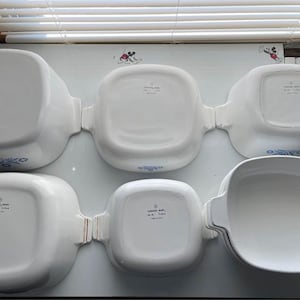 May include: A set of six white ceramic baking dishes with blue floral designs. The dishes are various sizes and shapes, including round, oval, and square.