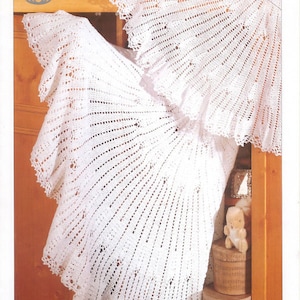 以下が含まれることがあります： 白いレース編みのベビーブランケットで、フリルが付いています。ブランケットは折り畳んで木製の表面に置かれています。画像の右上隅にはパターン番号3747が表示されています。画像の左上隅には「Sirdar Snuggly 2 Ply, 3 Ply Crochet」というテキストも表示されています。