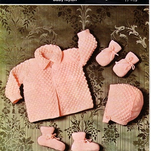 May include: A pink knitted baby set includes a cardigan, hat, and booties. The set is made of nylon and is designed for a baby aged 17 to 19 inches. The pattern is called "Cadette Quick Knit Baby Nylon" and is from Copley.