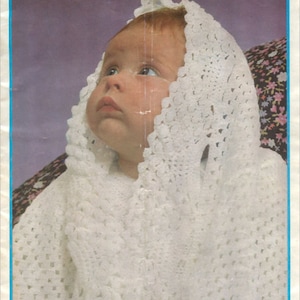 May include: A white crocheted baby bonnet with a scalloped edge. The bonnet is worn by a baby looking up. The image is from a vintage crochet pattern book.