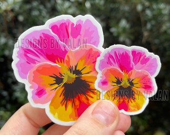 Könnte beinhalten: Zwei bunte Blumensticker mit rosa, gelben, orangen und schwarzen Akzenten. Die Sticker zeigen den Text "Designs by Valan".