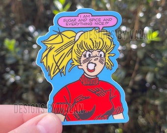 Peut inclure: Un autocollant de dessin animé d'une fille aux cheveux blonds et un pull rouge. L'autocollant a une bulle de dialogue qui dit "Je suis du sucre et des épices et tout ce qui est agréable !"