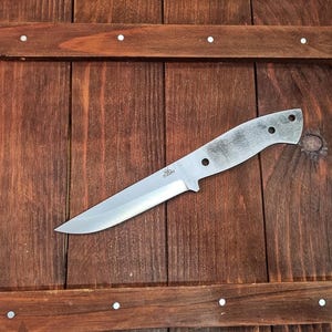 Può includere: Un coltello in acciaio inossidabile con una lama argentata e un manico grigio. Il coltello ha una punta e tre fori nel manico. Il coltello è appoggiato su una superficie di legno.