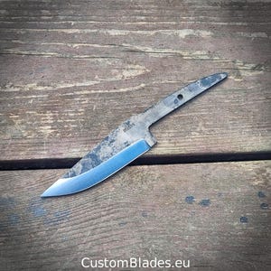 Op de afbeelding: Een metalen mesblad met een donkere, getextureerde afwerking op de rug en angel, voorzien van een gepolijste, scherpe snede. Het blad is gestempeld met de tekst 'blades' bij de bolster en de tekst 'CustomBlades.eu' is eveneens zichtbaar.