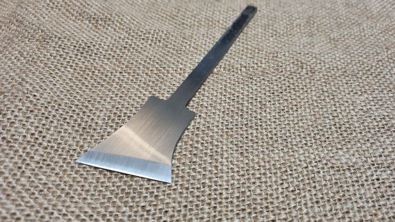 May include: A silver metal scraper tool with a long, thin handle. The blade is shaped like a small axe and has a sharp edge.