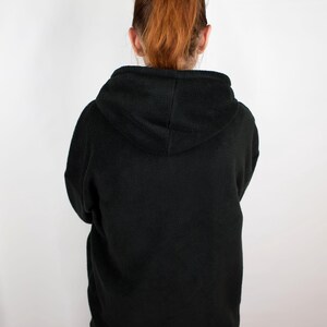 May include: A black fleece hoodie with a hood. The hoodie is pulled up and the hood is covering the person's head.