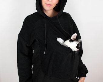 May include: A black fleece hoodie with a large pocket on the front, designed to hold a pet. A black and white cat is sleeping in the pocket.