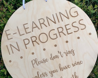 May include: A round wooden sign with the text "E-LEARNING IN PROGRESS" and a message below that reads "Please don't ring unless you have wine or teach math".