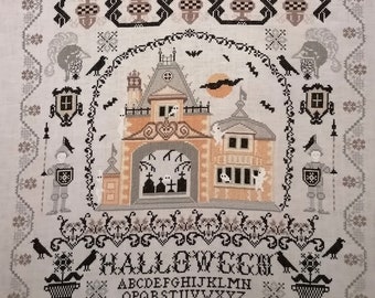 May include: A black and white cross-stitch pattern featuring a spooky Halloween house with ghosts, bats, and a graveyard. The pattern includes the word "HALLOWEEN" and an alphabet with numbers 20 and 23.