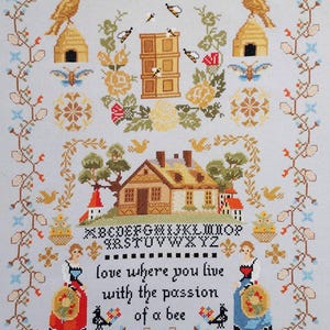 以下が含まれることがあります： 薄い青色の背景にクロスステッチのサンプル。家、蜂、鳥、花の要素がデザインされています。「love where you live with the passion of a bee」と書かれています。