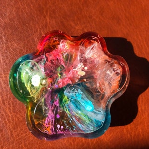 May include: A multi-colored resin dish with a paw print shape. The dish has swirls of pink, blue, green, and white resin.