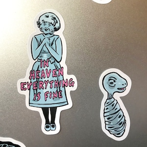 K&ouml;nnte beinhalten: Eine Sammlung von Aufklebern mit skurrilen Illustrationen. Ein Aufkleber zeigt eine Figur in einem blauen Kleid mit dem Text "IN HEAVEN EVERYTHING IS FINE". Ein anderer zeigt eine stilisierte, au&szlig;erirdische Kreatur. Die Aufkleber haben einen wei&szlig;en Rand.