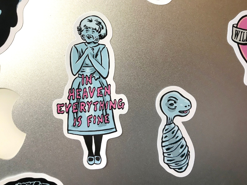 K&ouml;nnte beinhalten: Eine Sammlung von Aufklebern mit skurrilen Illustrationen. Ein Aufkleber zeigt eine Figur in einem blauen Kleid mit dem Text "IN HEAVEN EVERYTHING IS FINE". Ein anderer zeigt eine stilisierte, au&szlig;erirdische Kreatur. Die Aufkleber haben einen wei&szlig;en Rand.