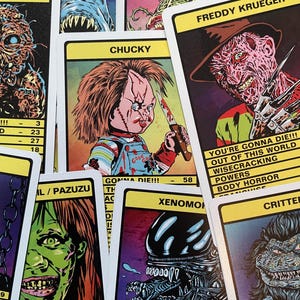 May include: A set of trading cards featuring various horror movie characters, including Chucky, Freddy Krueger, and the Xenomorph. Each card has a colourful illustration of the character and includes text about their powers and abilities. The cards are printed on a white background with black borders.